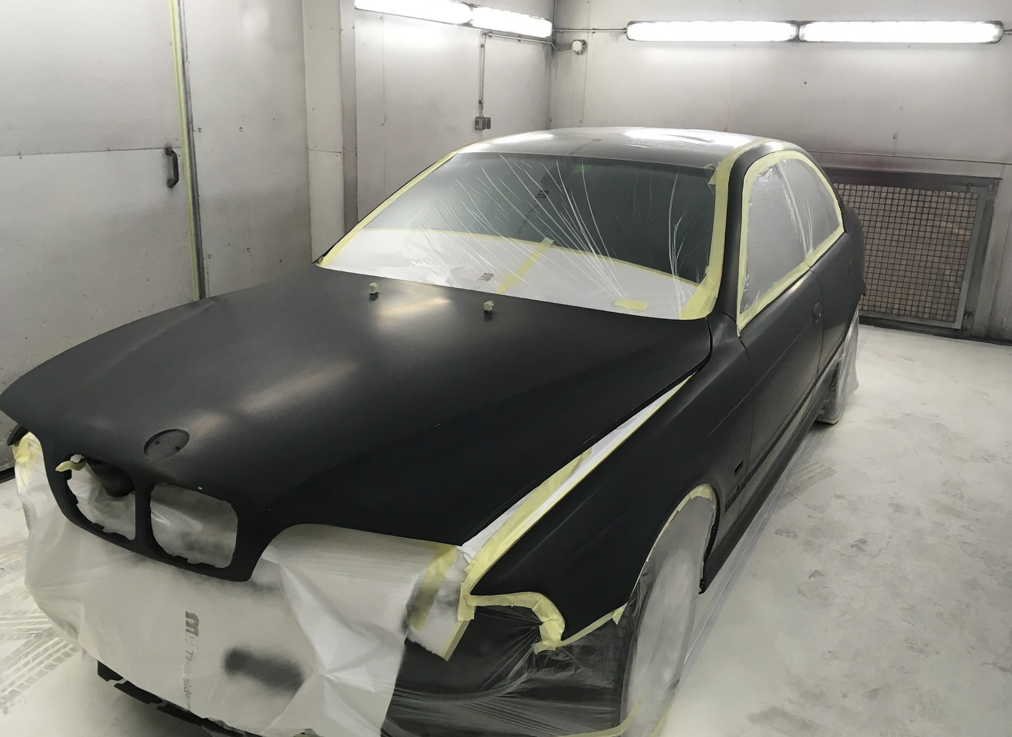 Zwarte BMW in de spuitcabine, afgeplakt voor het spuiten